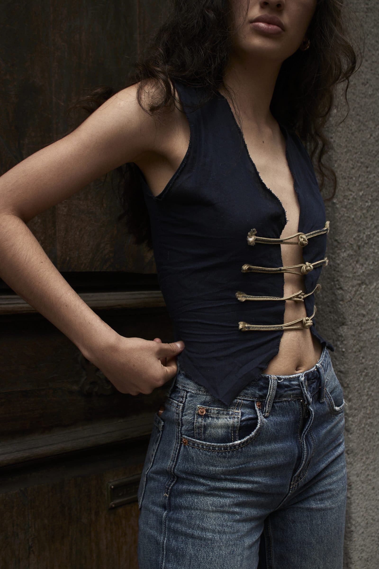 Model in the AYO waistcoat with brass toggles, against a dark wooden door